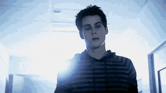 a young man in a striped shirt is standing in a hallway with a light shining on him .