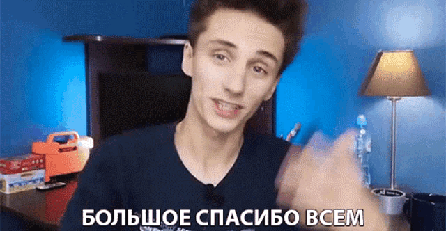a young man is giving a thumbs up in a room with a lamp and the words " большое спасибо всем "