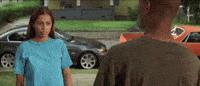 a man and a woman are standing next to each other in front of a house and cars .