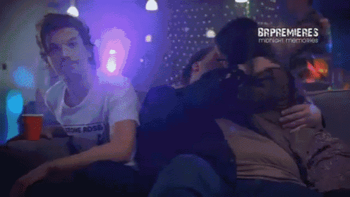 a man wearing a rolling ross shirt is sitting on a couch with two other people