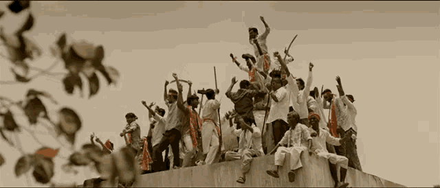 a group of people standing on top of a concrete wall with their arms in the air