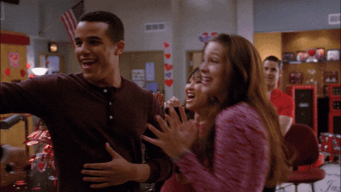a group of people are laughing and hugging in a room with hearts on the wall