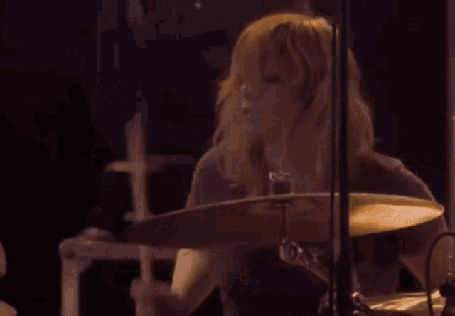 a woman is playing a drum set on a stage in a dark room .