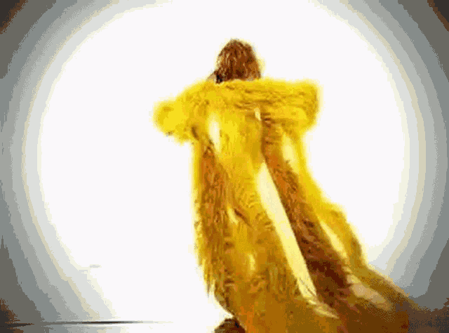 a woman in a long yellow fur coat is standing in a white room .