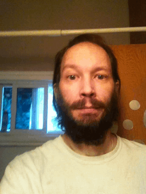a man with a beard and a white shirt looks at the camera