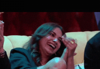 a woman is laughing while sitting on a couch with a glass in her hand