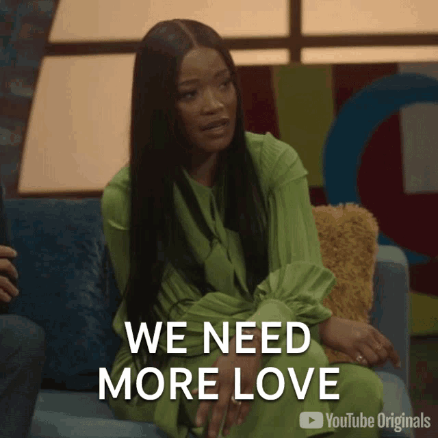 a woman in a green dress sits on a couch with the words " we need more love " behind her