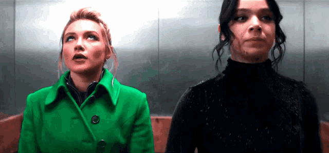 a woman in a green coat is standing next to another woman in a black sweater .