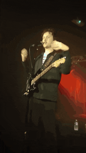 a man playing a guitar and singing into a microphone with his hands in the air