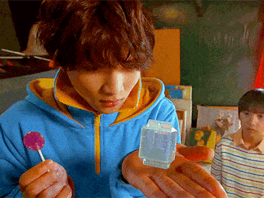 a man in a blue jacket is holding a purple lollipop and a small cube