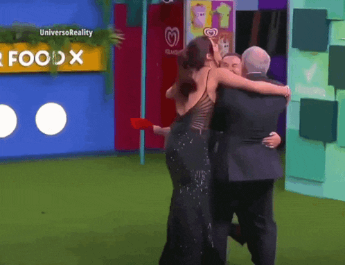 a woman in a black dress is hugging two men in front of a sign that says universoreality
