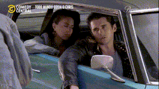 a man and a woman are sitting in a car with comedy central on the bottom right