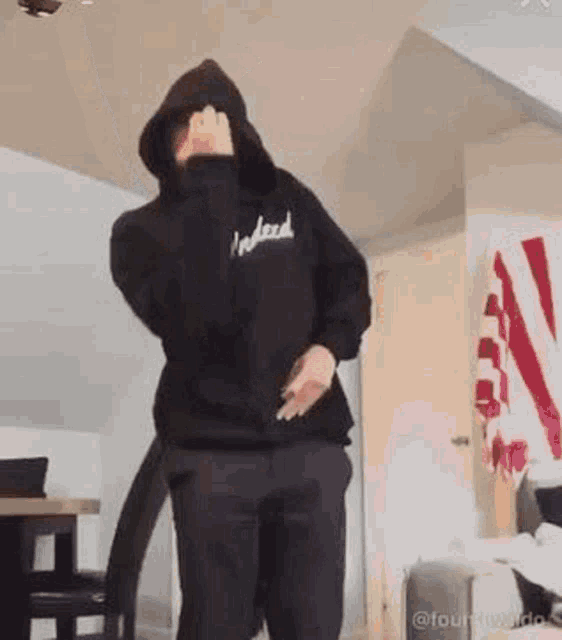 a man wearing a black hoodie and black pants is dancing in a living room .