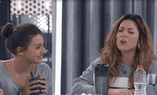 two women are sitting next to each other with a bottle of water in front of them .