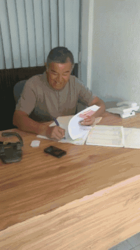 a man sits at a desk writing on a piece of paper with a pen