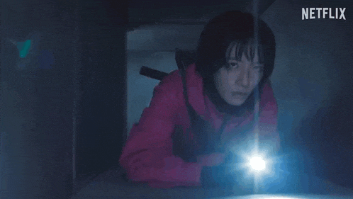 a woman in a red jacket is holding a flashlight in the dark .