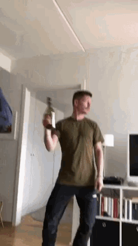 a man in a green shirt is dancing in a living room while holding a bottle