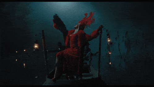 a woman in a red dress is sitting in a boat in the dark