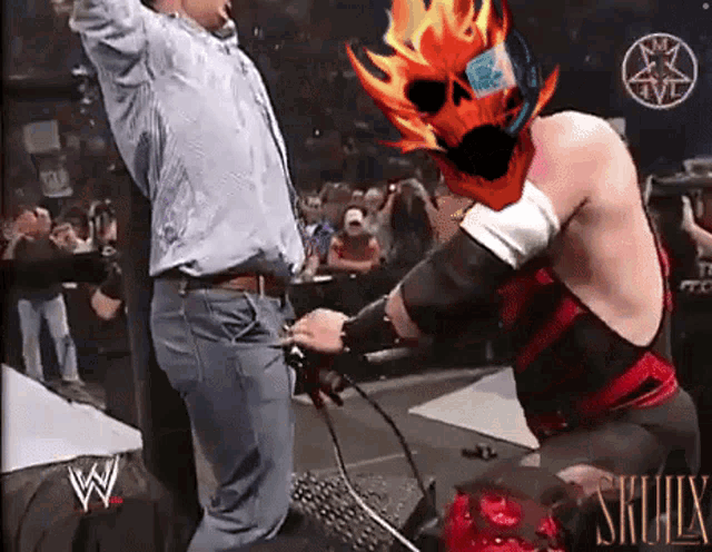 a man in a blue shirt is standing next to a wrestler in a red and black outfit with skullx written on his chest