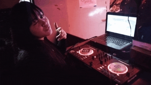 a woman sitting in front of a pioneer dj controller and a laptop