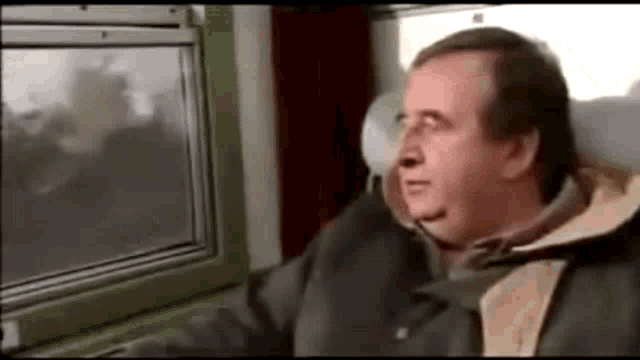 a man is sitting on a train and looking out the window .
