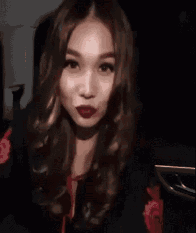 a woman with long hair and red lipstick is sitting in a car and making a funny face .