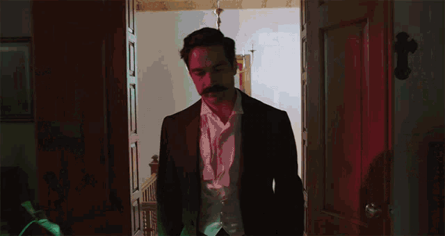 a man with a mustache in a suit is standing in a doorway