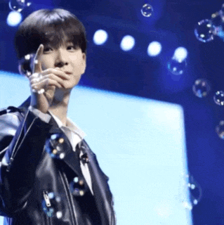 a young man in a black leather jacket is standing in front of soap bubbles .