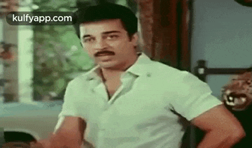 a man with a mustache is standing in a room with his hands on his hips and looking at the camera .