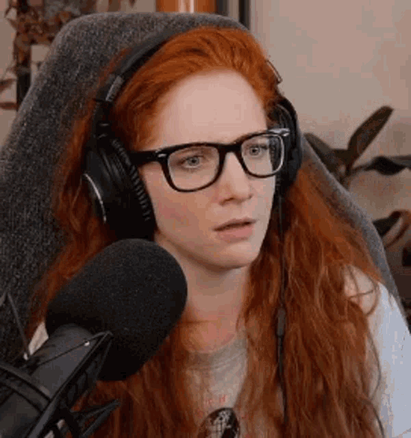 a woman with red hair is wearing headphones and glasses while sitting in front of a microphone .