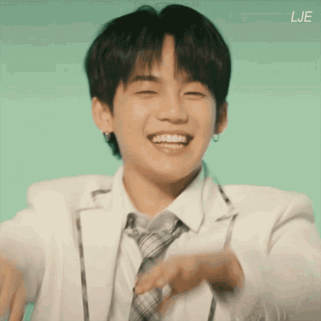 a young man wearing a white jacket and tie is smiling and making a funny face .