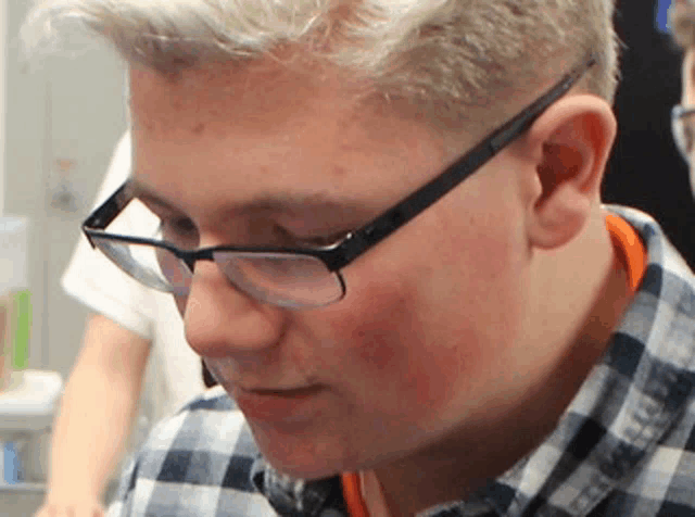 a young man wearing glasses and a plaid shirt looks down