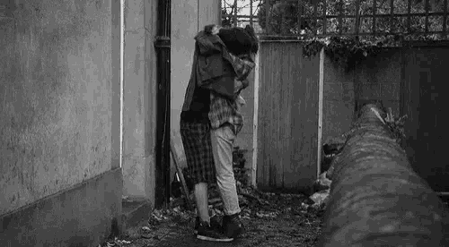 a black and white photo of a man and woman hugging each other in front of a building .