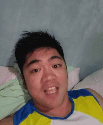 a man in a blue and yellow shirt is making a funny face while laying on a bed .