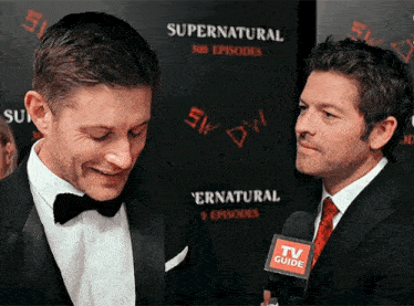 two men are standing next to each other in front of a supernatural poster
