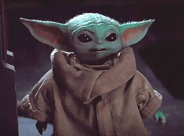 the baby yoda from star wars is wearing a scarf around his neck and looking at the camera .