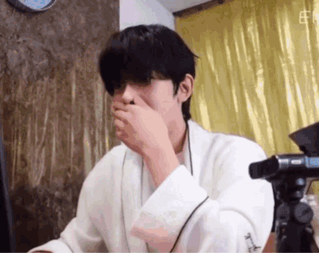 a man wearing a white robe is covering his mouth with his hand while sitting in front of a computer .