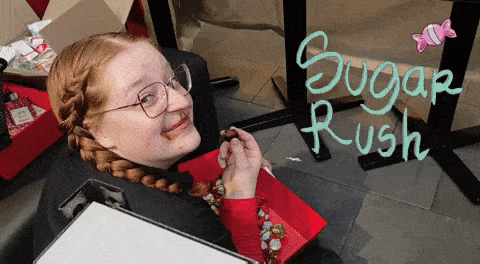a girl with glasses is eating a piece of chocolate with the words sugar rush written on the wall behind her