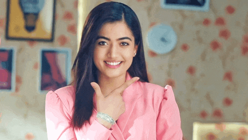 a woman in a pink jacket is smiling and pointing