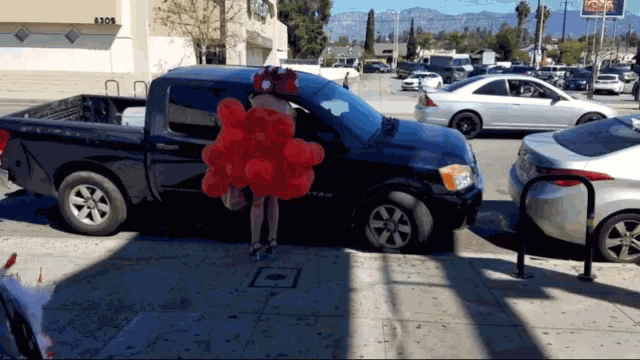 a woman holding a bunch of red balloons in front of a truck