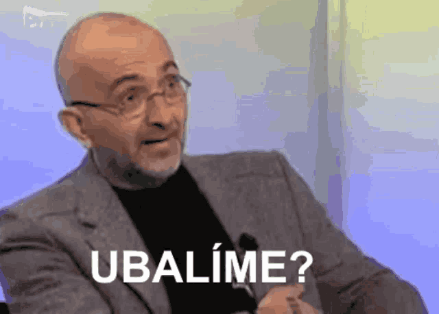 a man in a suit and glasses says ubalime while sitting in front of a microphone