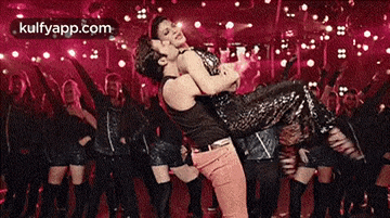 a man is holding a woman in his arms in front of a crowd of dancers .