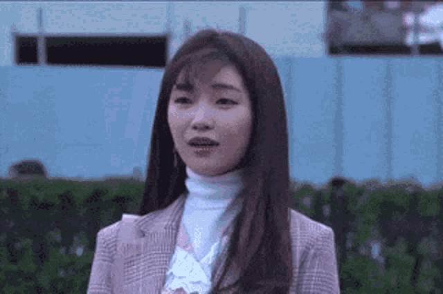 a woman wearing a plaid jacket and a white turtleneck is standing in front of a fence .