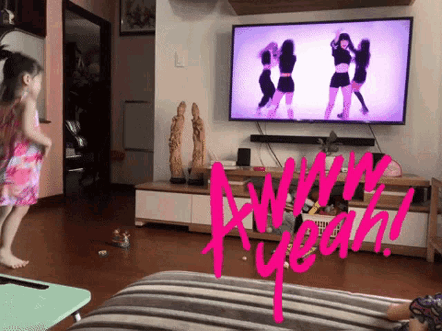 a little girl is jumping in front of a tv that says yeah on it