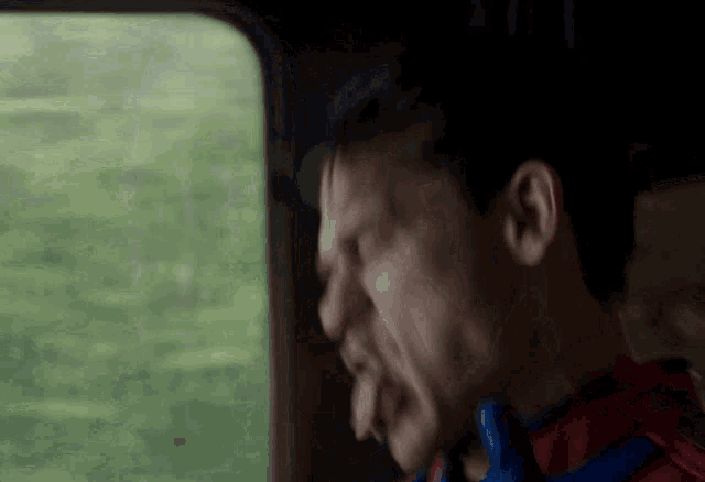 a man in a superhero costume is sticking his tongue out while looking out a window .
