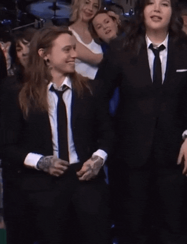 two women in suits and ties are holding hands in front of a crowd .