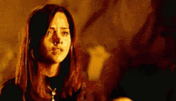 a woman with long brown hair is looking at the camera with a serious look on her face .