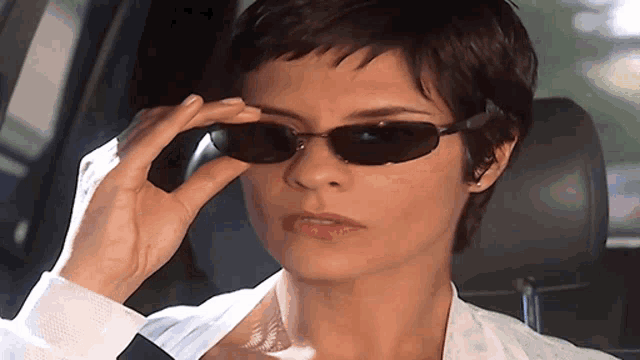 a woman wearing sunglasses looks at the camera with a serious look on her face