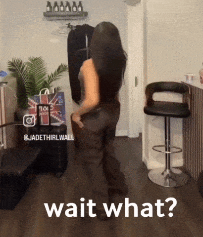 a woman is standing in a room with the words wait what on the bottom right