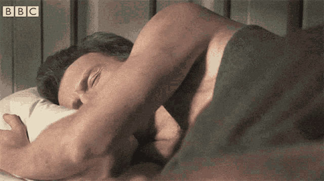 a shirtless man is sleeping in a bed with bbc written on the corner